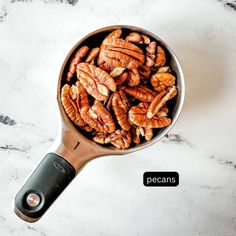 a spoon full of pecans sitting on top of a white counter next to a black and silver measuring cup