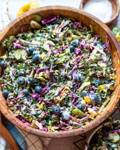 a wooden bowl filled with blueberries, cabbage and other vegetables next to lemon wedges