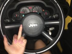 a woman driving a car with her hand on the steering wheel and pointing at it