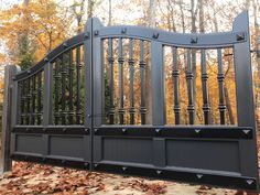 an iron gate in front of trees with leaves on the ground