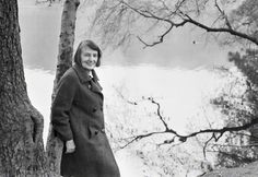 an old photo of a woman standing next to a tree by the water's edge