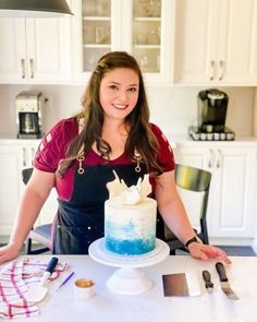 a woman standing in front of a cake on top of a white kitchen table with utensils