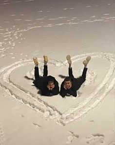 two people laying in the snow making a heart shape