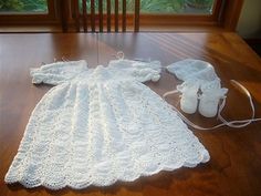 a white crocheted baby dress and booties on a wooden table with a window in the background