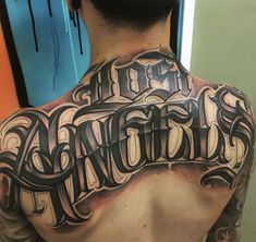 the back of a man's upper half covered with tattoos and lettering that spell out his name