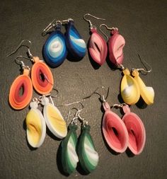 six pairs of colorful earrings are arranged in a circle on a black surface with silver earwires