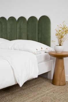 a white bed sitting next to a wooden table with a vase on top of it