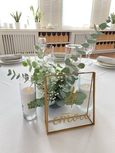 the table is set with candles, plates and vases filled with greenery on it