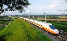 a high speed train traveling down the tracks near a lush green field with trees and power lines in the background