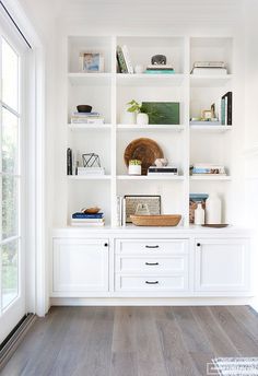 a living room with white bookcases and wood flooring on the side wall