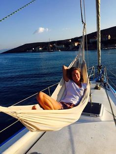 a woman sitting in a hammock on the back of a sailboat looking at the camera