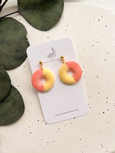 a pair of pink and yellow donut earrings sitting on top of a white plate