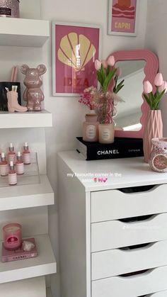 a white dresser topped with lots of drawers and vases filled with pink flowers next to a mirror