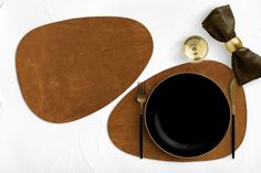 a place setting with black plates and silverware on a white table cloth, next to a brown napkin