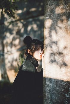 a woman standing next to a tree with her hand on her face and shadow cast on the wall behind her