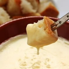 a spoon full of cheese dip with bread in the background and dipping sauce on it