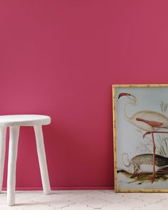 a pink wall with two white stools in front of it and a painting on the floor