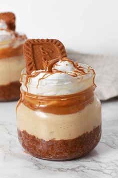 two dessert jars with cookies and whipped cream in them on a marble countertop, one has an oreo cookie