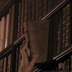 a hand is holding an old book in front of a bookshelf full of books