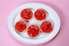 four strawberry shortbreads on a white plate with red icing and strawberries