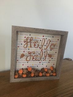 a wooden frame with some pine cones and acorns in it on a table