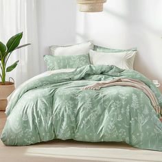 a bed with green comforters and pillows in a room next to a plant on the floor