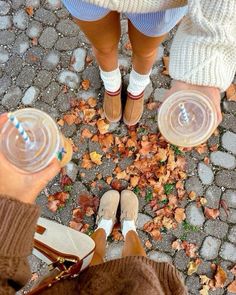 two people standing next to each other with their feet on the ground holding plastic cups