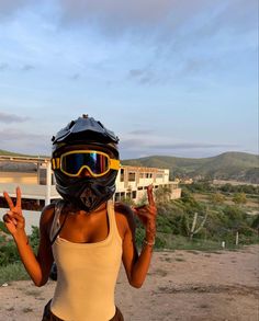 a woman wearing a helmet and goggles standing in front of a building with her fingers up