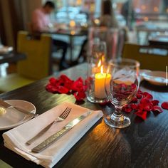 the table is set with silverware and rose petals on it, next to a candle