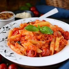 a white plate topped with pasta covered in sauce and tomato sauce next to some tomatoes