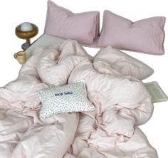 an unmade bed with pink sheets and pillows on it, next to a lamp