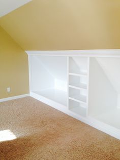 an empty room with yellow walls and white shelving unit in the corner on top of carpeted floor