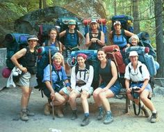 a group of people with backpacks and hiking gear posing for a photo in the woods