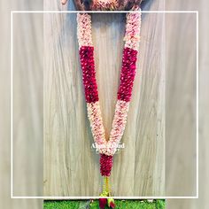 a long necklace with pink and white flowers hanging from it's side on a wooden wall