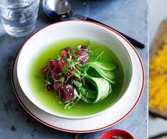 a bowl of green soup on a table next to two bowls of food and spoons