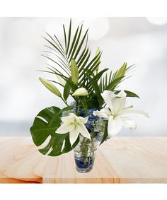 a vase filled with white flowers sitting on top of a wooden table covered in greenery