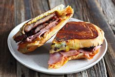 a ham and egg panini cut in half on a white plate with a wooden table