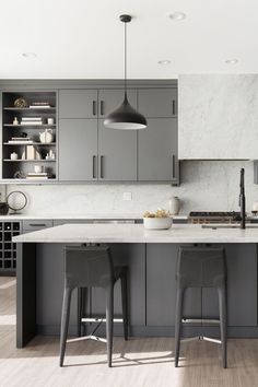 two stools are in front of an island with marble countertops and gray cabinets