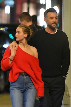 the man and woman are walking down the street together, both wearing red sweaters