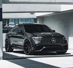 a black mercedes suv parked in front of a white building with concrete walls and columns