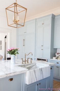 a white kitchen with marble counter tops and gold faucet hanging from the ceiling