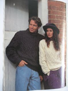 two people standing next to each other in front of a door wearing sweaters and hats