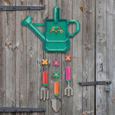 a green watering can with gardening tools hanging from it's side on a wooden fence