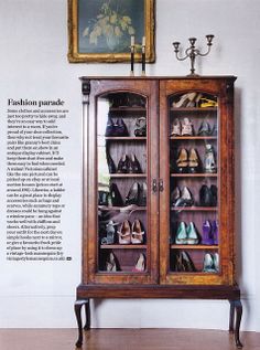 a wooden cabinet filled with lots of pairs of shoes next to a painting on the wall