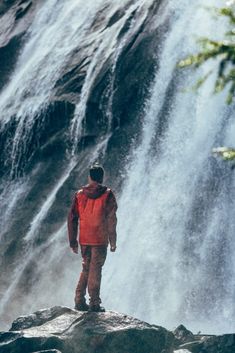 a man standing on top of a rock next to a waterfall