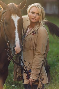 a woman standing next to a brown and white horse