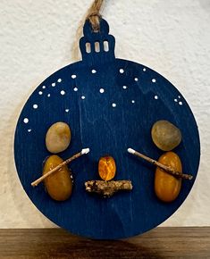 a blue ornament with rocks and sticks on it hanging from a rope in front of a white wall