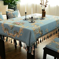 a blue table cloth with tassels and flowers on it in front of a window