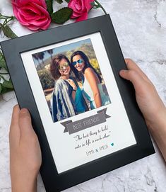 a person holding up a framed photo with pink roses in the background and an image of two women on it