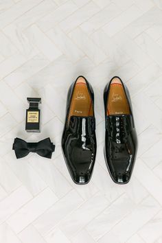 a pair of black shoes and a bottle of perfume on a white tile floor next to a bow tie